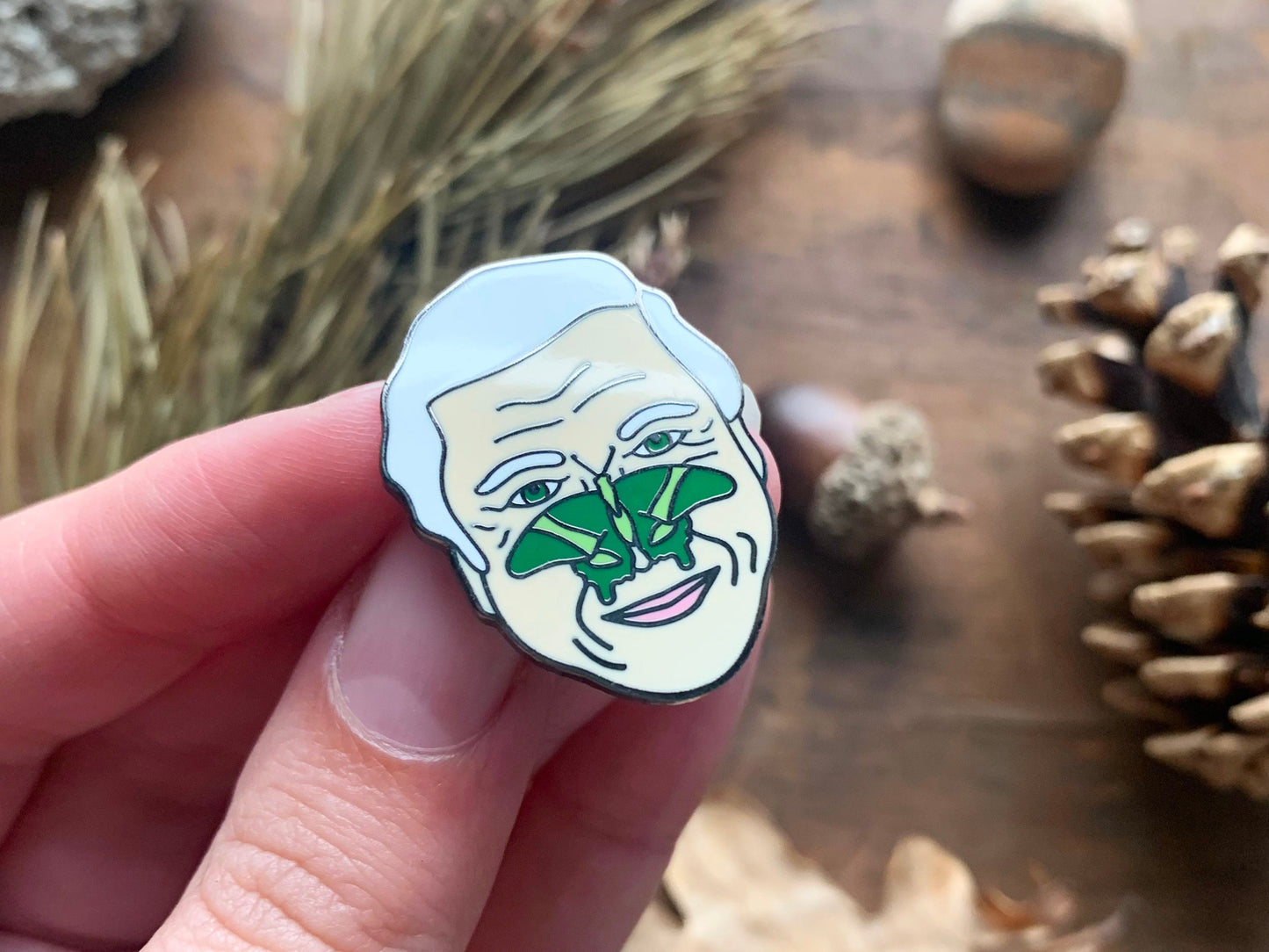 Enamel pin of Sir David Attenborough with a green butterfly on his face.