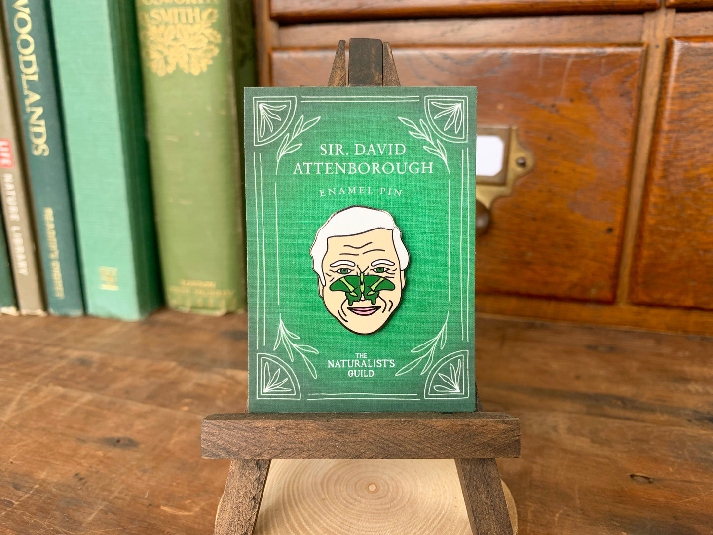 Enamel pin of Sir David Attenborough with a green butterfly on his face.