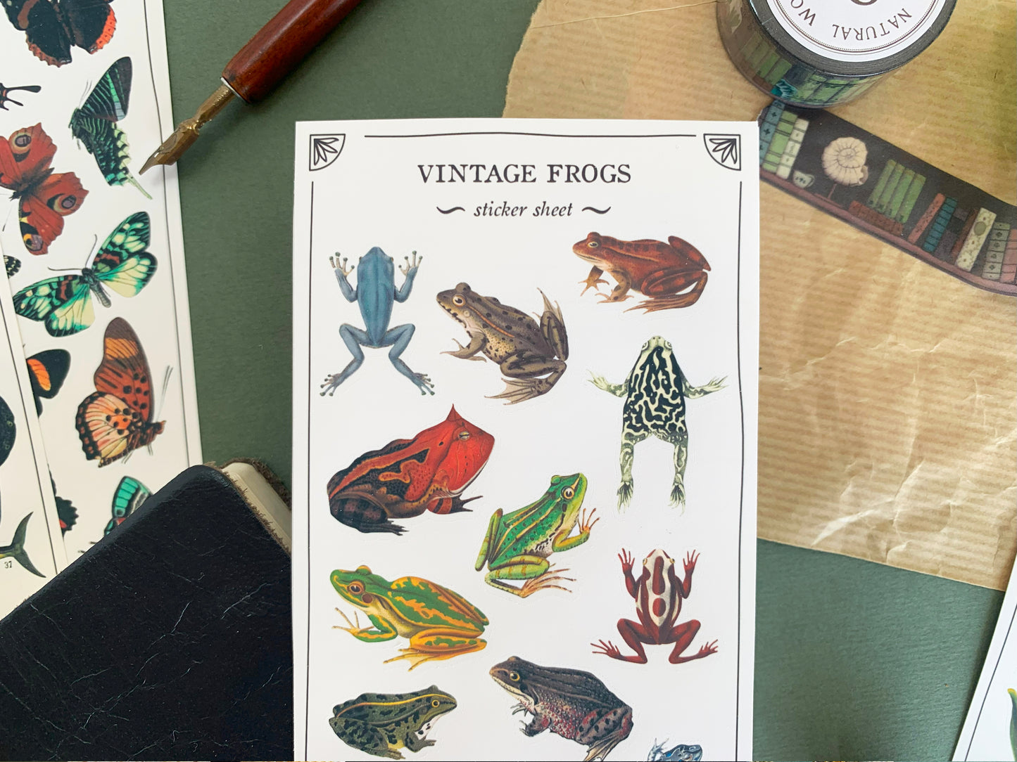 Close up of a sticker sheet of butterfly species in a detailed and colourful vintage illustration style, with stationery in the background. The Naturalist's Guild.